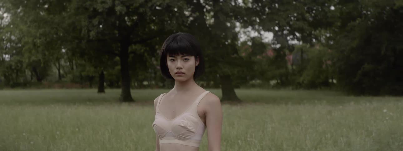 Asian woman wearing brassiere stands on the lawn looking at camera