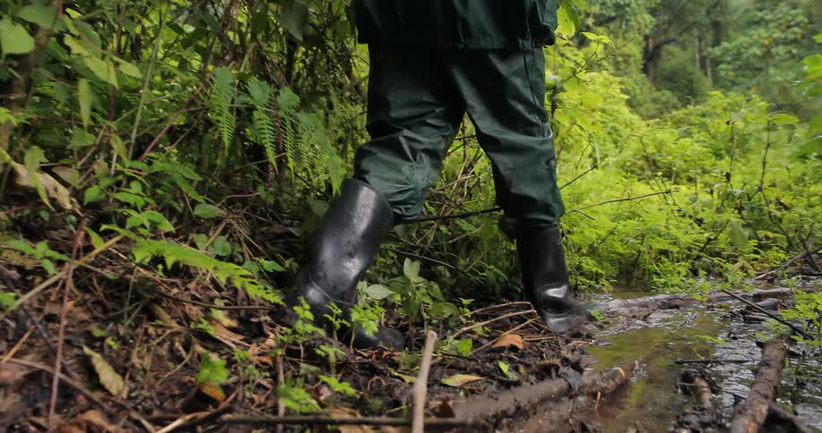 A hiker in rain boots walks across a wet and muddy area