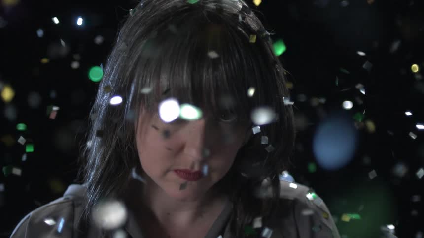 Woman stares as large bits of reflective paper fall around her