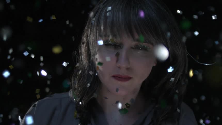 Colorful shimmering confetti floats and rises around a woman wearing glittery eyeshadow