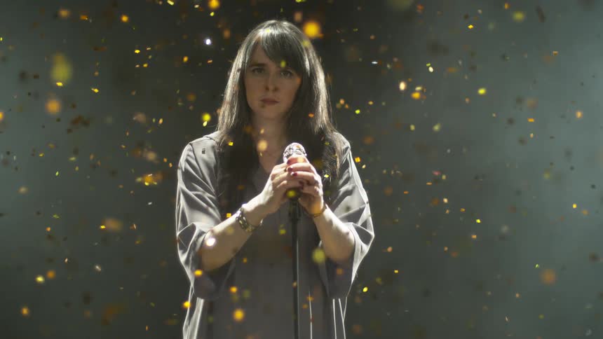 Woman stands at microphone with gold confetti falling