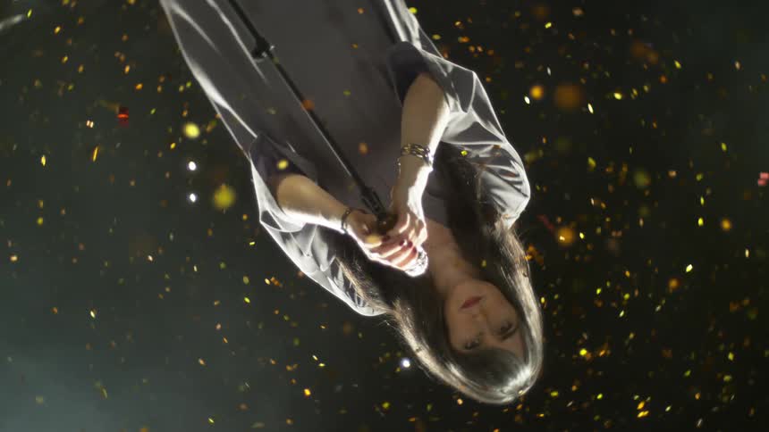 Woman standing at microphone surrounded by gold confetti