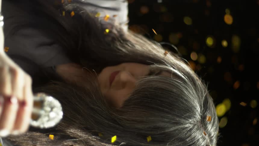 A white woman holds a shiny object in her hand as glitter falls around her