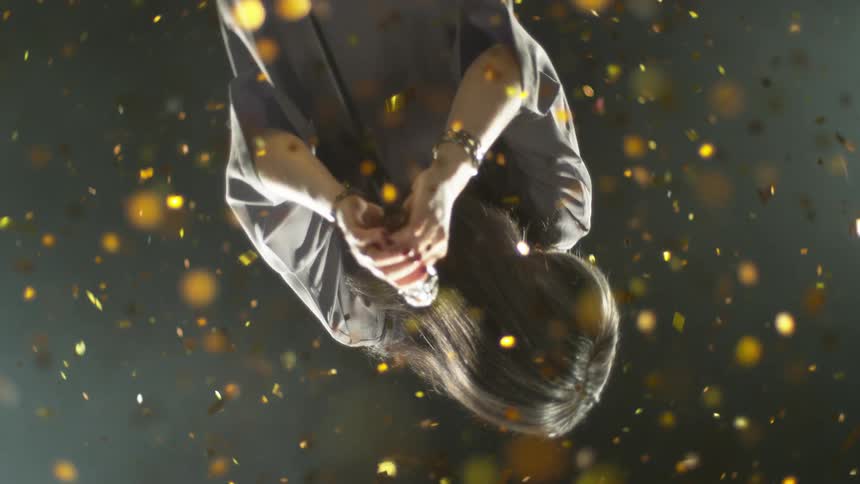 Woman with microphone surrounded by falling gold confetti