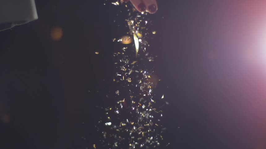 Confetti and glitter falls from a white womans hand
