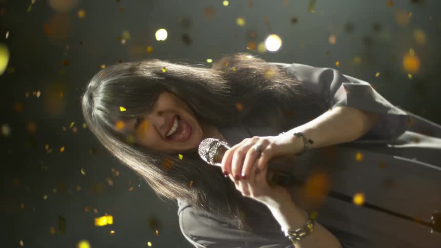 Young woman with microphone surrounded by falling gold glitter