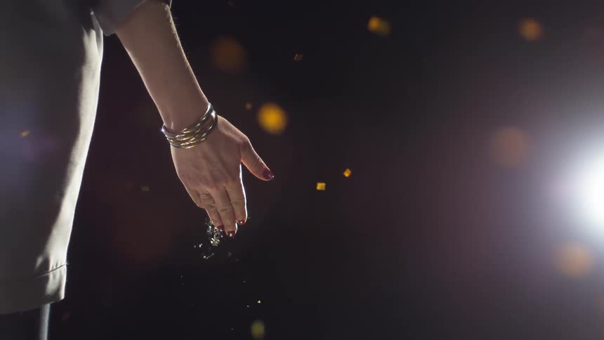 A person drops glitter in front of a spotlight