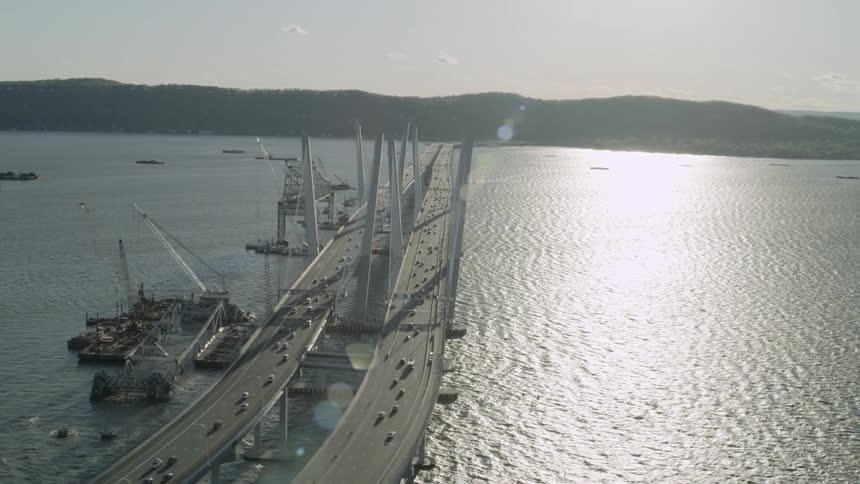 Construction cranes in the water by a bridge as cars drive across