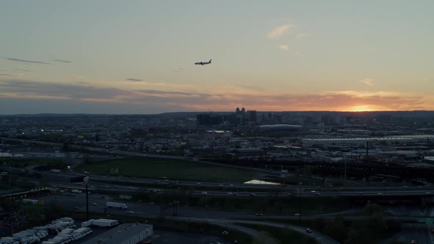 An airplane flies over a city and a network of highways filled with cars and trucks