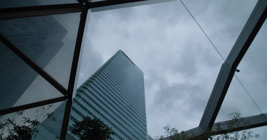 A camera circles while staring straight through a glass ceiling to a nearby skyscraper