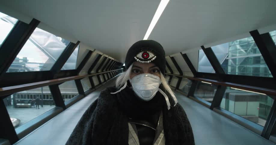 A white woman wearing a mask stands in an elevated enclosed walkway