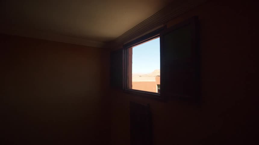Window in dimly lit room show roof of and persons in another building