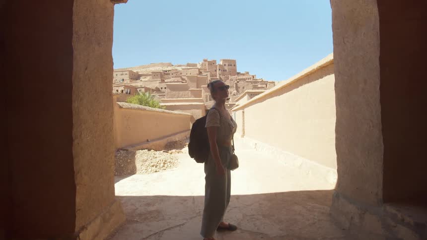 Female tourist stands at the entrance to a cement building under a blue sky