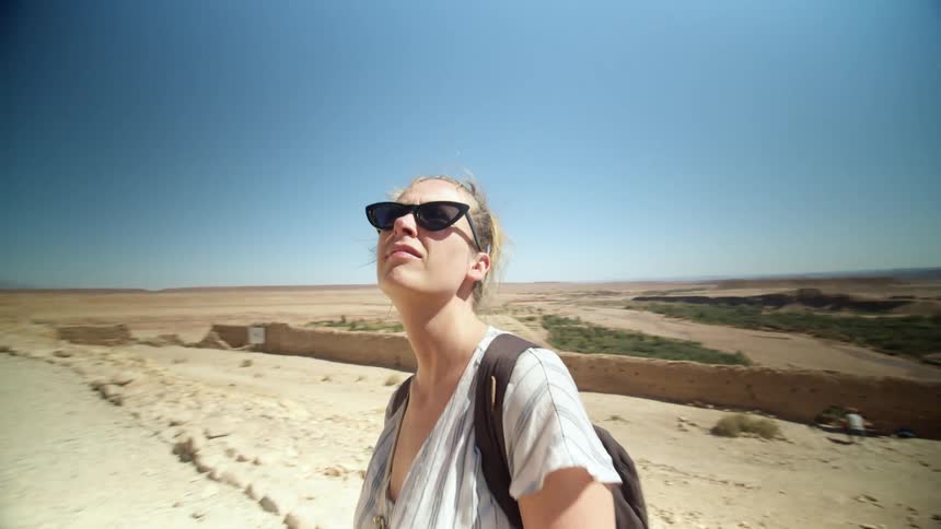 A woman stands on a path in the desert and looks around