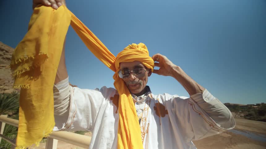 A man puts a turban on as people cross a bridge and go towards him