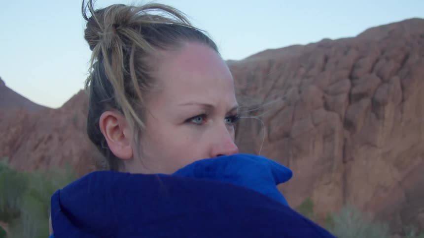 A woman wears a blue scarf like a cape and wraps it around her chest
