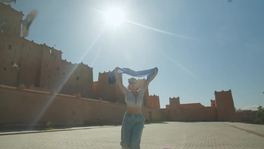 A woman in front of a building holding a blue scarf running and making pigeons fly away