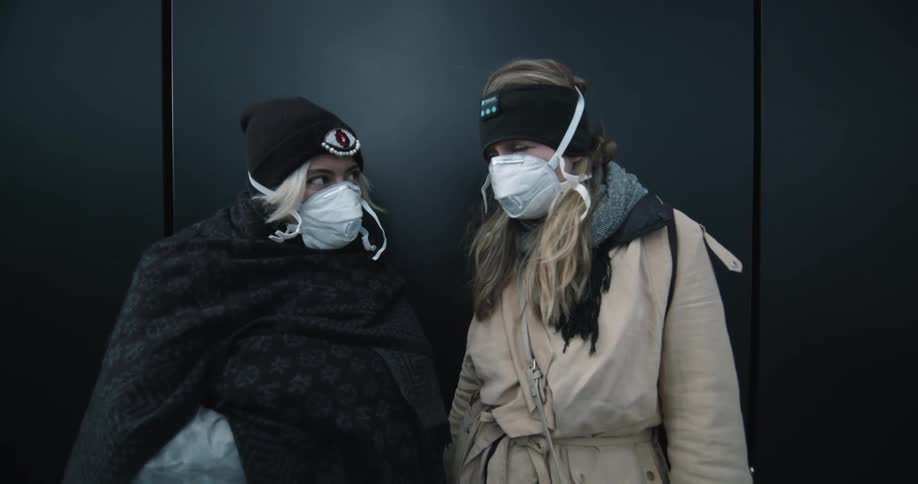 Two women wearing face mask and coat stand near each other