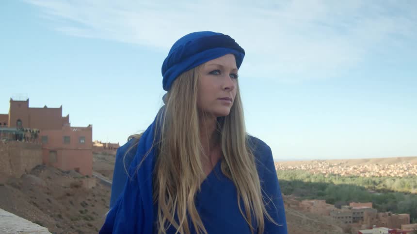 A woman standing and looking around with a village behind her
