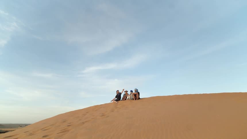 Four friends sit on top of a sand dune in a desert