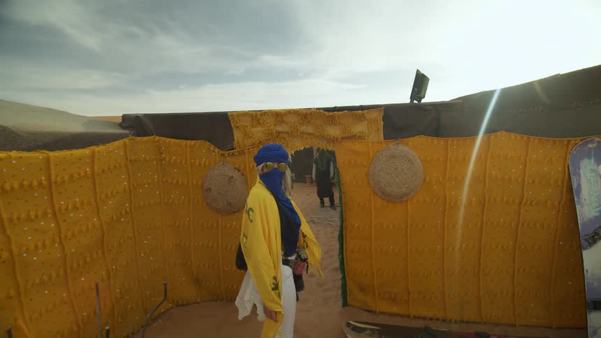 Woman with her face covered walks near a tent in the desert