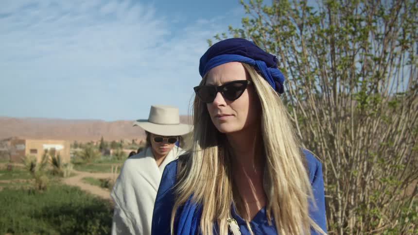 A white woman leads a procession of other people down a dirt path in a field