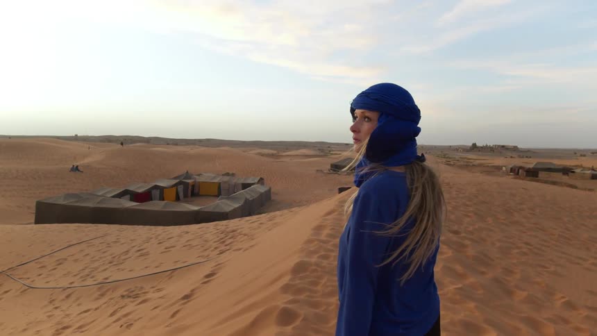 Young woman standing on sand dune overlooking nomadic tent village in desert