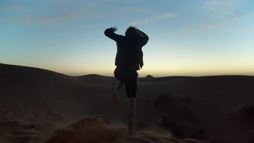 Person runs and jumps from sand dune in desert at dusk