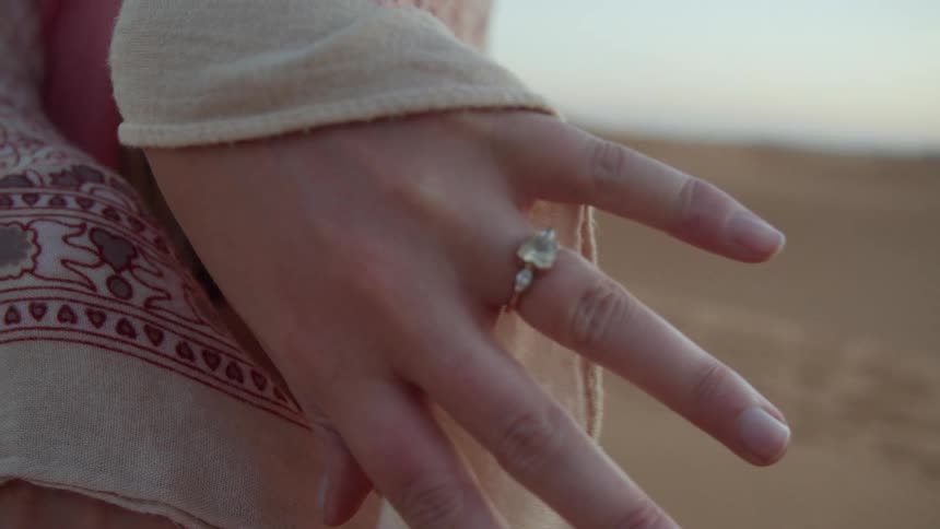 A white woman shows off the ring on her finger while standing out in a desert