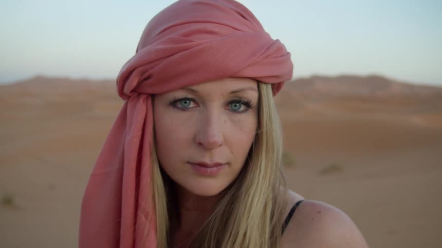 Blonde woman wearing a scarf poses for the camera in the desert