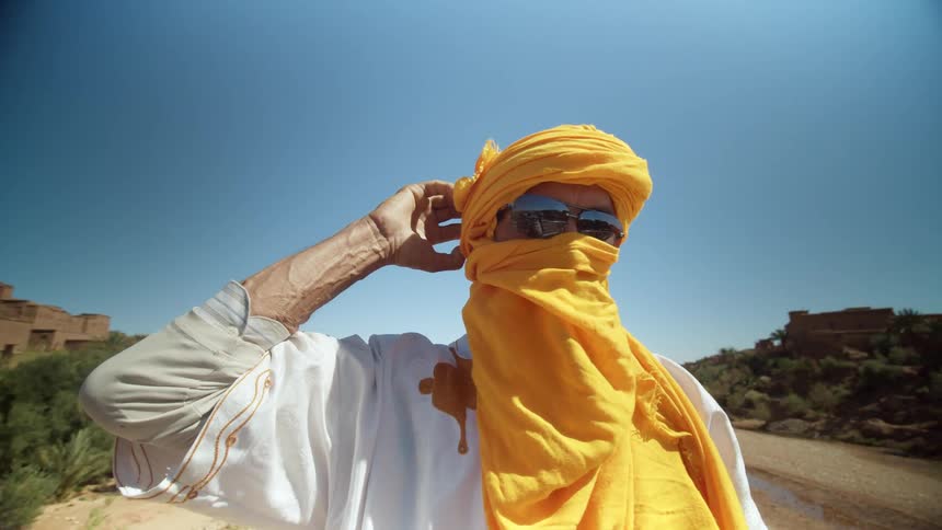 A man wearing a yellow turban stands on a pedestrian bridge in the desert