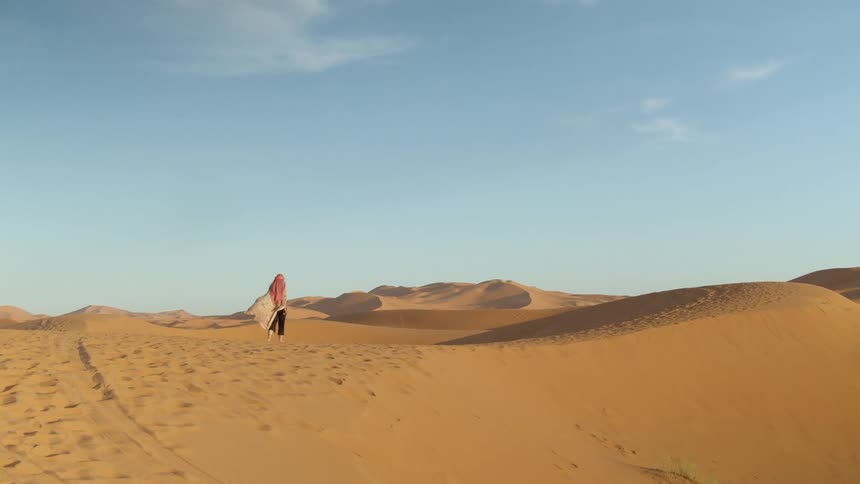 A white woman walks over sand dunes in a desert