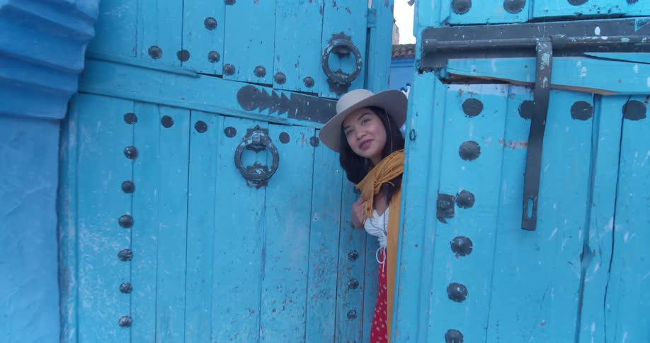 Young woman looking through large light blue city gate