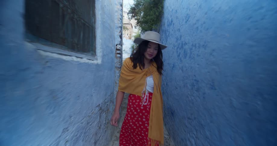 Woman wearing a brimmed hat walks on the narrow path between two buildings