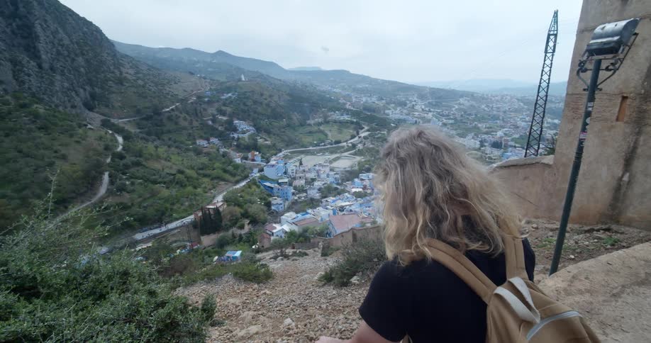A woman sits on top of a hill and looks down at houses in a neighborhood
