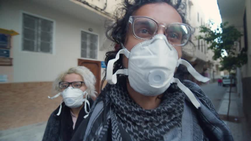 Two women with face masks walk through a narrow street in a neighborhood