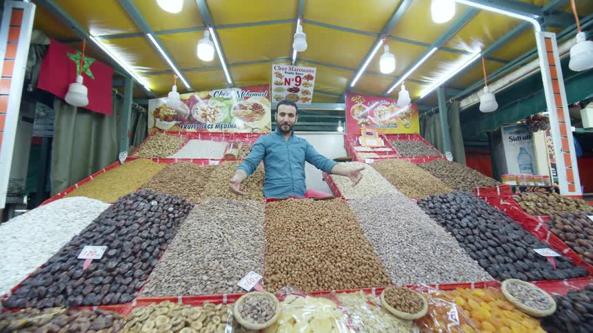 A man who works at a market speaks and offers a piece of food