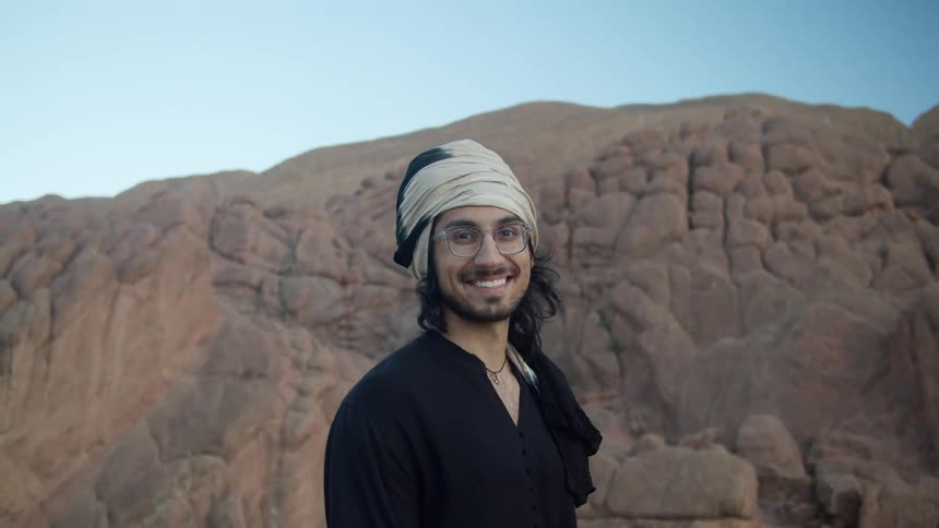 A man standing outdoors in front of a low mountain and smiling into the camera