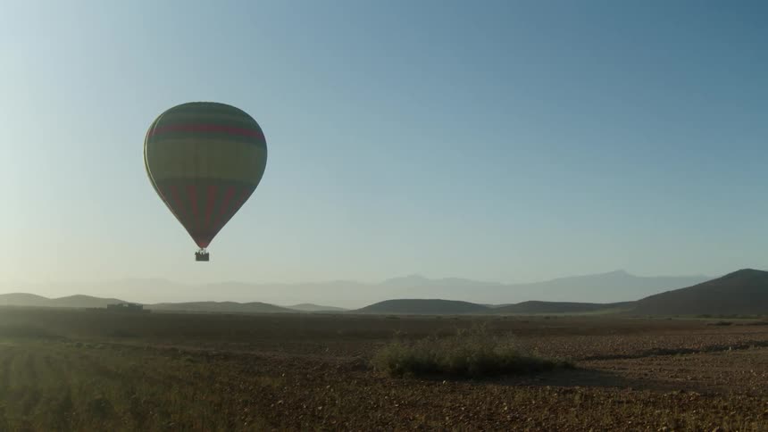 A hot air balloon hovers an expanse of flat land