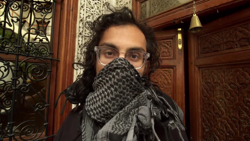 A man standing in front of a building with a scarf over his face