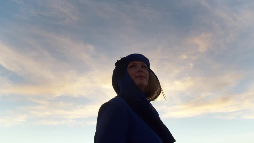White woman wearing a blue scarf stands and looks around in the desert