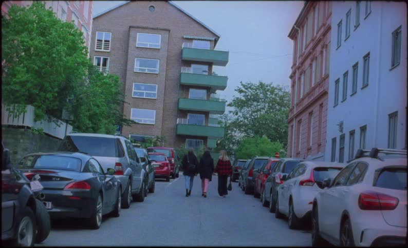 Three women walk down the middle of a neighborhood street filled with parked cars