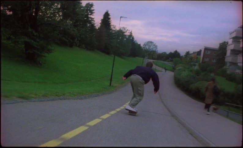 A group of young men skateboarding quickly down a hill while doing tricks and avoiding pedestrians