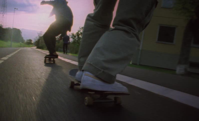 Three young males skateboard down a suburban road