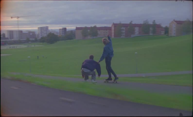 A group of three males rides skateboards down a small back road