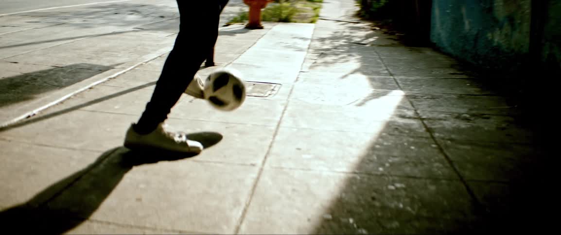 A teenager kicks a soccer ball on a sidewalk in a neighborhood