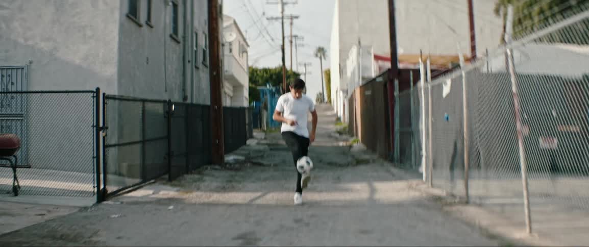 A hispanic man plays around with a soccer ball in an alley