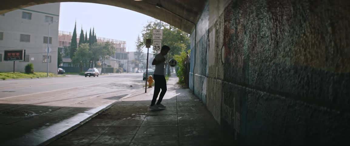 Man dribbles soccer ball against wall near tunnel exit as car passes