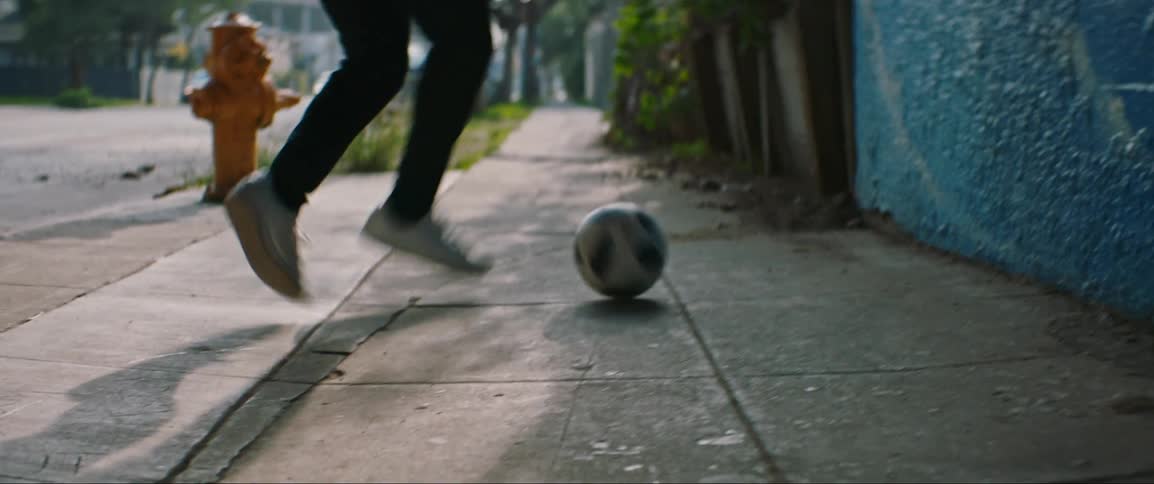 A boy kicks a soccer ball down a city sidewalk