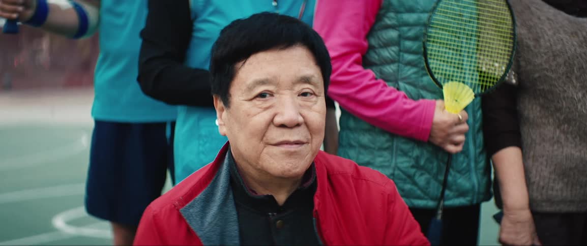 A man sitting and staring with people holding badminton rackets behind him